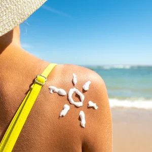 Mulher na praia com desenho de sol em creme na pele, representando a categoria de cosméticos de verão Prom Cosmetics